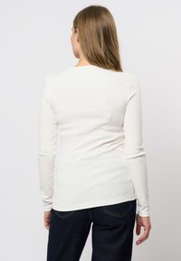 Top alb cu mâneci lungi, din material texturat, cu un design ajustat și guler rotund, combinat cu blugi negri. Vederea din spate arată un material neted.