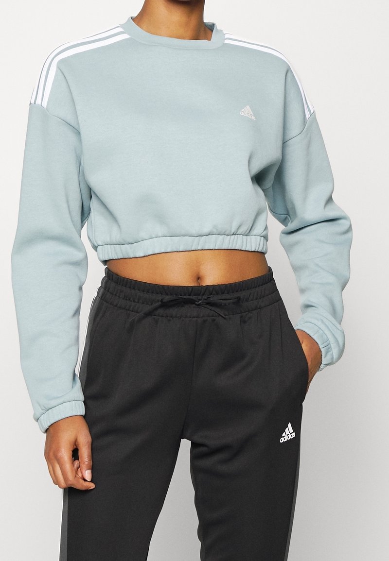 Helles blaues, cropped Sweatshirt mit weißen Streifen auf den Schultern und elastischem Saum. Kombiniert mit schwarzen Jogginghosen mit elastischem Bund.