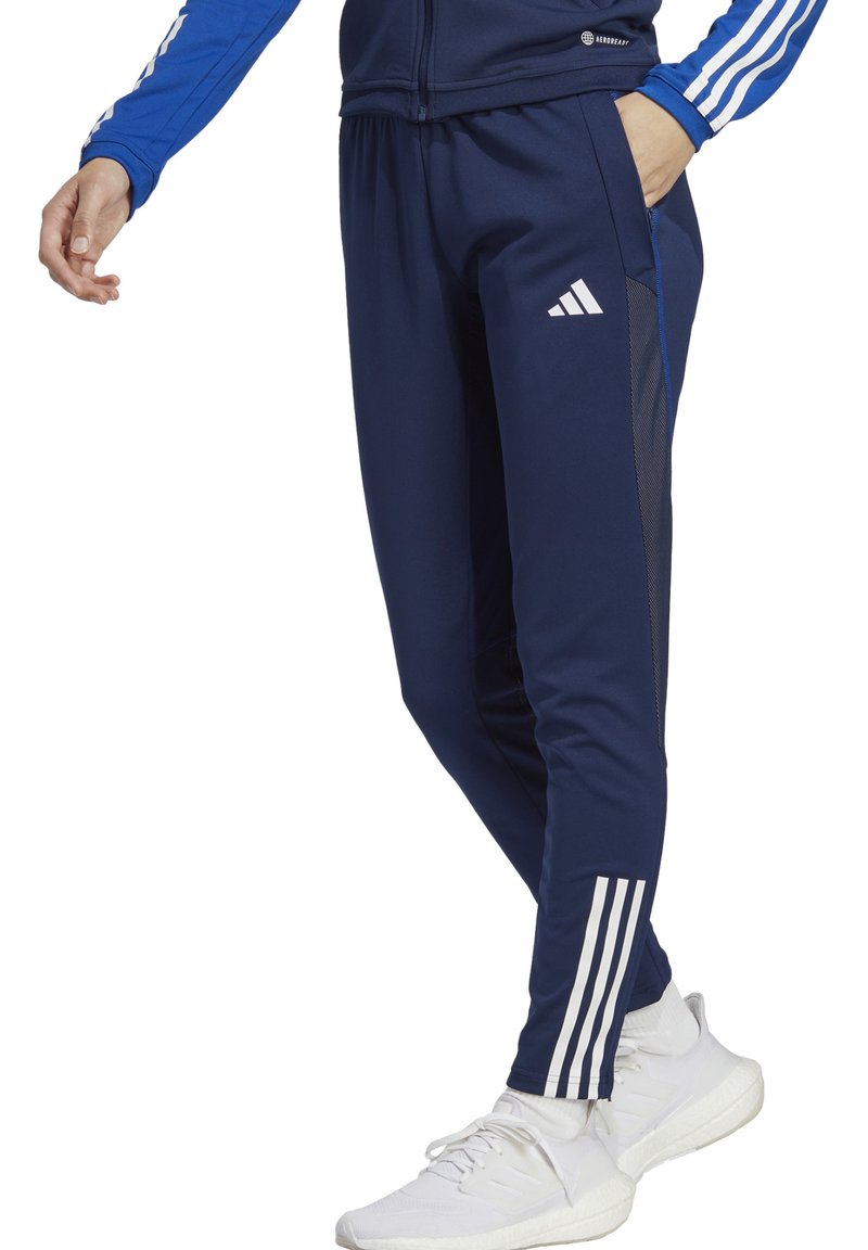 Pantalons de sport bleu marine avec un design ajusté, présentant des rayures blanches Adidas sur les côtés et un panneau en maille, complétés par une taille élastique.