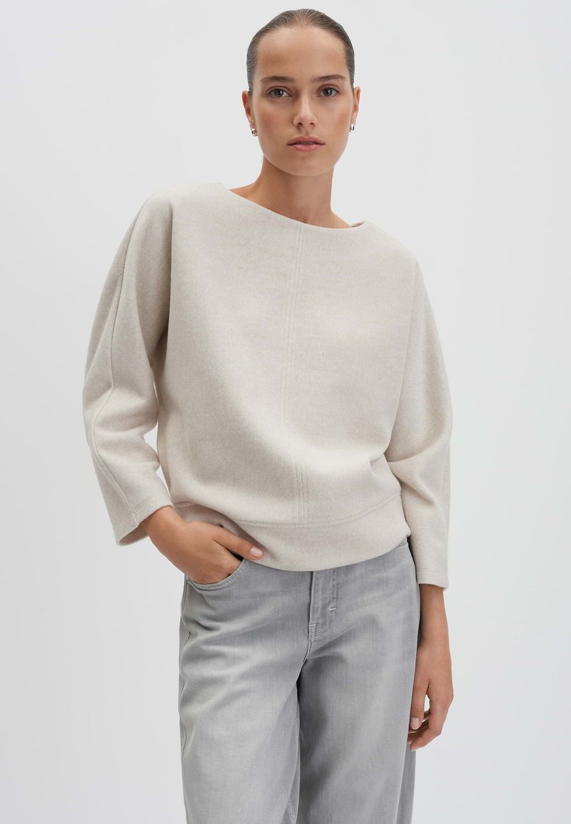Pullover beige chiaro con una vestibilità comoda, scollo ampio e maniche a tre quarti, abbinato a pantaloni grigio chiaro con vestibilità rilassata. Tessuto morbido.