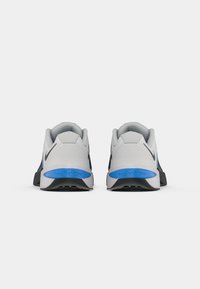 Pair of white and blue Nike Metcon sneakers shown from the back, featuring black swoosh logos and textured soles.
