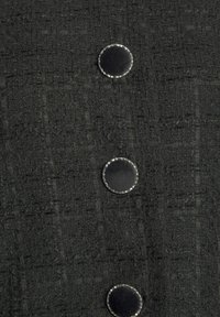 Trois boutons en tissu noir recouverts de tissu avec une bordure argentée sur un tissu tissé gris foncé texturé.
