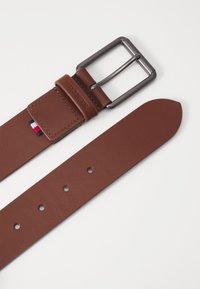 Ceinture en cuir marron avec une boucle en métal argenté, dotée d'une boucle en cuir marquée et de plusieurs trous pour l'ajustement de la taille.
