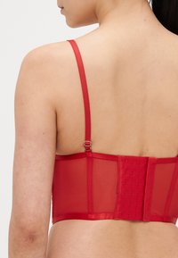 Soutien em rede vermelha com alças ajustáveis, fecho de gancho nas costas, textura suave e suporte estruturado.