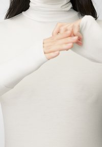 Langsleeve coltrui in zacht witte stof met aansluitende mouwen. Heeft een hoge hals en gerolde textuur bij de kraag. Soepele, minimalistische vormgeving.