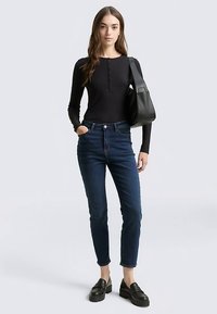 Svart ribbad långärmad topp med knappdetaljer, kombinerad med höga mörkblå jeans och svarta platåloafers. Svart axelväska.