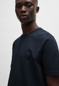 Navy blue t-shirt in soft cotton with a round neckline, featuring a square black logo patch with "BOSS" on the chest.