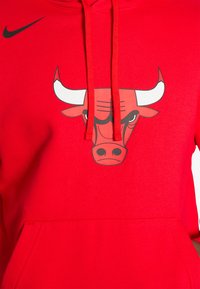 Červená mikina s kapucňou vyrobená z fleecu s klokanie vreckom, zdobená grafikou hlavy býka v čierno-bielej farbe. Logo Nike v čiernej farbe na hrudi.