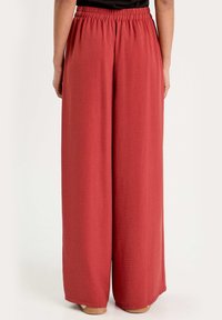 Pantalons larges rouges en tissu texturé léger. Ils possèdent une taille élastique confortable et tombent jusqu'aux chevilles.