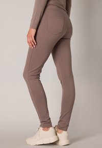 Bruine stretch legging met een aansluitend ontwerp, middelhoge taille en achterzakken. Draagt met lichtgekleurde sneakers. Glad textuur.