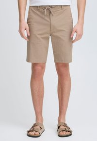 Beige katoenen shorts met een trekkoord in de taille, voorzakken en een rechte snit; gecombineerd met tan sandalen met twee banden.