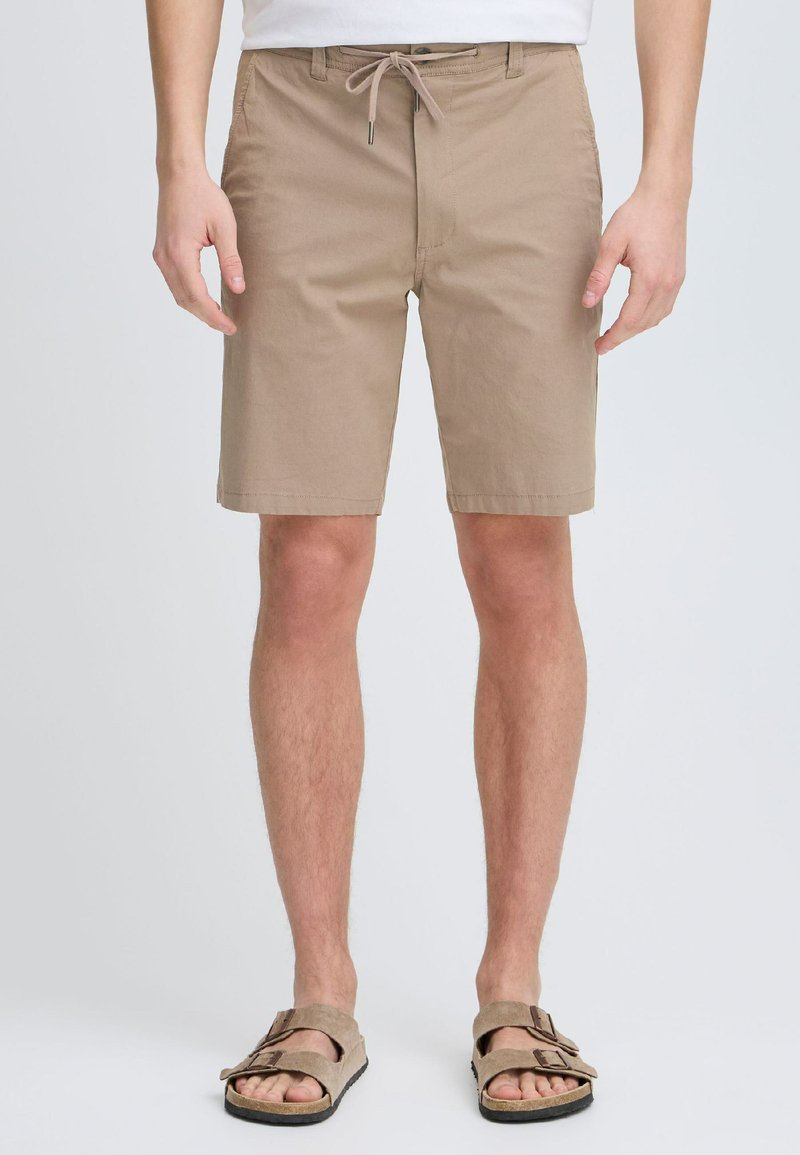 Beige katoenen shorts met een trekkoord in de taille, voorzakken en een rechte snit; gecombineerd met tan sandalen met twee banden.