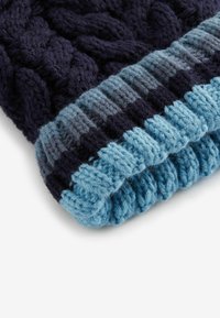 Gehaakte beanie in donker marineblauw en blauwe tinten; heeft een kabelpatroon met geribbelde rand; zachte, gestructureerde garen; warm winteraccessoire.