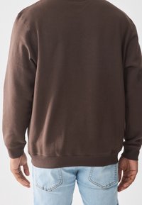 Sudadera de algodón marrón con cuello redondo, puños y dobladillo acanalados. Presenta una textura suave, diseño ajustado y estilo minimalista.
