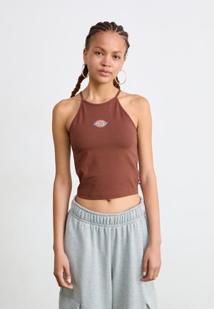 Braunes, kurzes Tanktop mit einem Halterneck-Design, das ein farbenfrohes "Dickies"-Logo zeigt. Das Model hat es mit grauen Jogginghosen kombiniert.