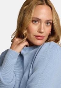 Pull tricoté bleu clair avec un col haut et une texture côtelée, doté de manches longues et d'une coupe décontractée.