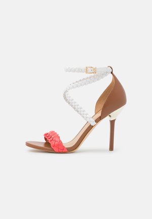 Sandale à talon haut avec un talon et une semelle marron, bride d’orteil tressée corail, brides de cheville tressées blanches et boucle dorée.