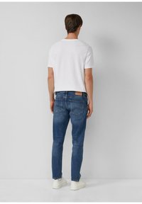 Biała koszulka z krótkim rękawem zestawiona z niebieskimi dżinsami i białymi trampkami. Dżinsy mają naszywkę z tyłu oraz dwie tylne kieszenie.