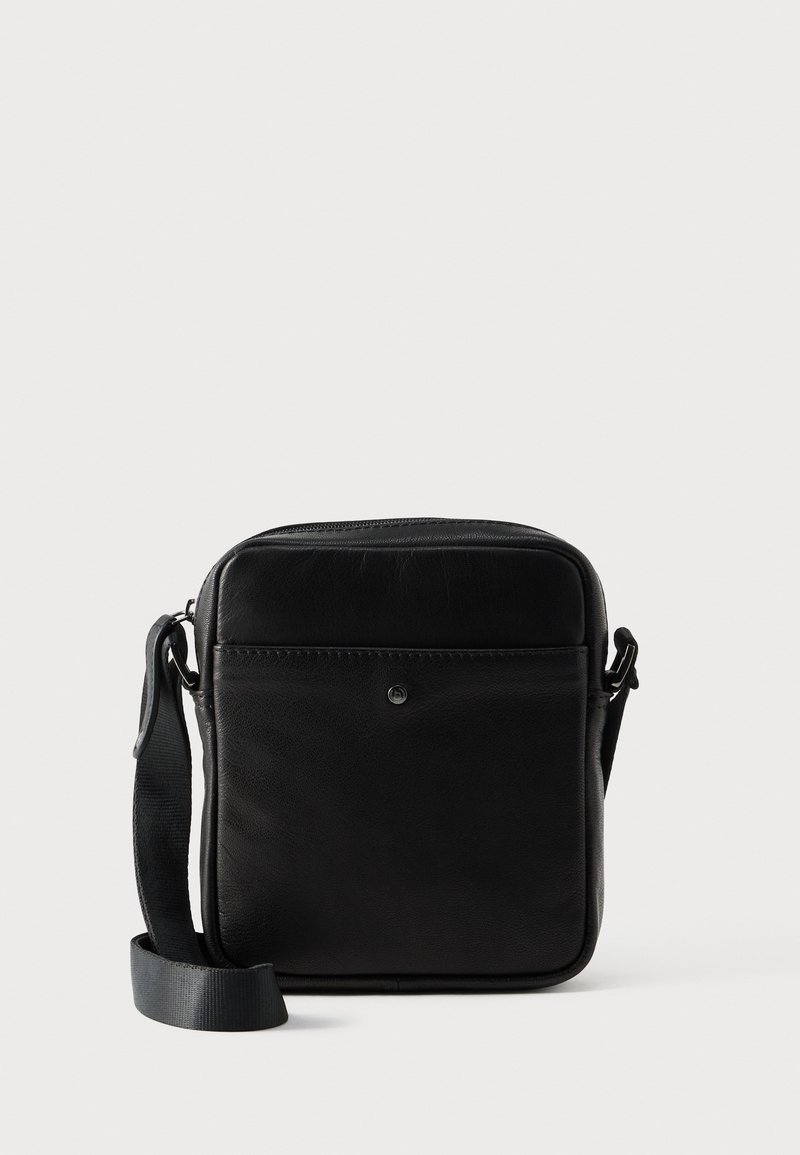 Μαύρο δερμάτινο τσαντάκι χιαστί με ομαλή υφή, ορθογώνιο σχήμα, ρυθμιζόμενο λουρί και μπροστινή τσέπη με φερμουάρ. Διαθέτει μινιμαλιστικό σχεδιασμό.