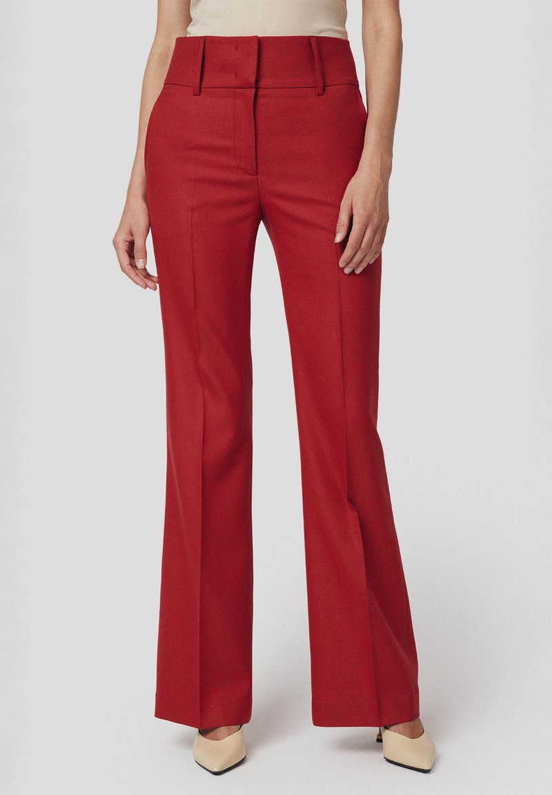 Czerwone rozszerzane spodnie z wysokim stanem, z detalicznym przeszyciem i kieszeniami bocznymi. Wykonane z gładkiego materiału, wykończone elegancką sylwetką.