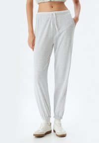 Grijze sweatpants met elastische tailleband en boorden, zijzakken en trekkoorddetails. Gemaakt in combinatie met witte sneakers met beige accenten.