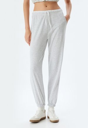 Grijze sweatpants met elastische tailleband en boorden, zijzakken en trekkoorddetails. Gemaakt in combinatie met witte sneakers met beige accenten.