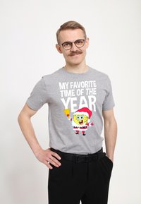 Šedé bavlněné tričko s barevným potiskem SpongeBoba SquarePanta v santovském kostýmu a výrazným bílým textem: "MOJE NEJOBLÍBENĚJŠÍ OBDOBÍ ROKU."