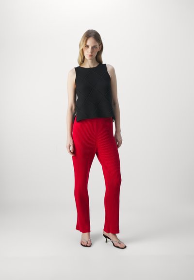 Schwarzes gestricktes Top mit einem strukturierten Rautenmuster, kombiniert mit roten gerippten Hosen und silbernen Absatzsandalen. Schlichtes, modernes Design.