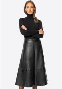 Jupe midi en cuir noir à silhouette évasée, avec une texture lisse et des détails de coutures. Associée à un col roulé noir ajusté.