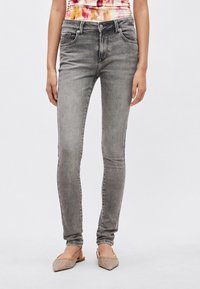 Szare obcisłe dżinsy z wyblakłą fakturą, przednimi kieszeniami i metalowymi elementami, zestawione z jasnobrązowymi butami na pasku z ozdobnymi akcentami.