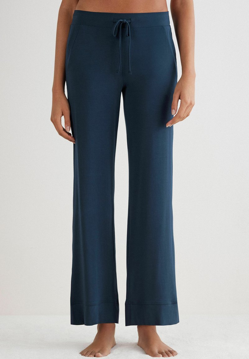 Granatowe spodnie dresowe z elastycznym paskiem, szerokimi nogawkami i gładką teksturą. Posiadają kontrastowe wykończenie szwem na dole.
