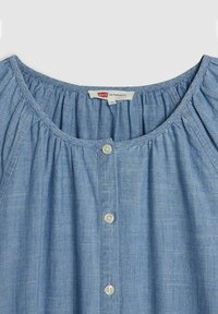 Vaaleansininen farkkupaita, jossa on koottu kaula-aukko, etupuolella kolme valkoista nappia ja tagi, jossa lukee "Levi's San Francisco, CA."