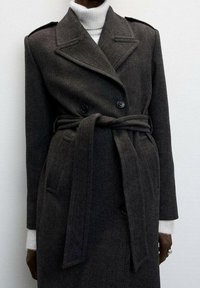 Trench-coat en laine à chevrons foncés avec un design croisé, des revers en encoche et une ceinture à nouer. Comprend des poches latérales et un tissu texturé.