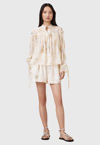Lightly patterned, cream blouse with gathered detailing, button closure, and long sleeves; paired with matching shorts, both in a silky fabric.