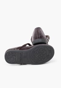 Scarpa in velluto marrone con punta arrotondata e una cinghia, dotata di una suola in gomma nera testurizzata con disegni floreali e a forma di cuore.