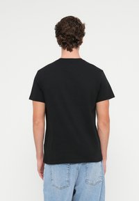 Czarna bawełniana koszulka z okrągłym dekoltem, krótkimi rękawami i luźnym krojem, noszona z jasnoniebieskimi dżinsami. Gładkie plecy.