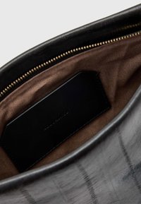 Borsa a tracolla in pelle nera con esterno liscio, caratterizzata da una fodera in tessuto marrone e un'etichetta in pelle nera all'interno. Chiusura con zip dorata.