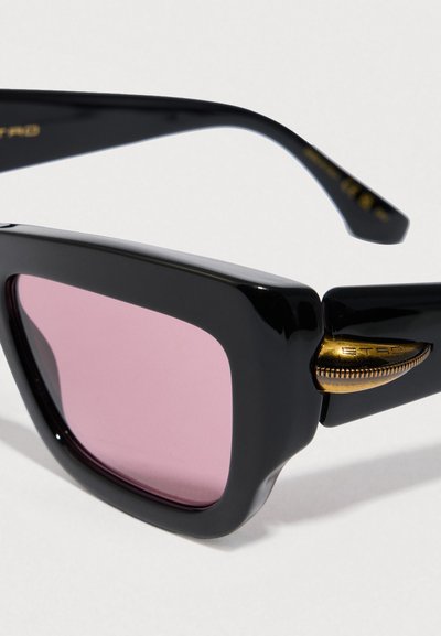 Occhiali da sole neri con finitura lucida, lenti rosa e dettagli in metallo dorato. Caratterizzati da un design angolare e montature spesse.