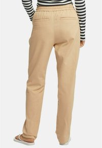 Beige byxor med elastisk midja, med två bakfickor och raka ben, som bärs med en randig långärmad topp.