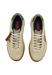 Scarpe da ginnastica beige con tomaia in tessuto testurizzato, dettagli verdi e marchio rosso. Presentano una suola in gomma color sabbia e lacci bianchi.