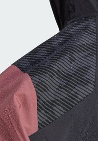 Tissu résistant à l'eau avec un motif ondulé noir, des sections en violet foncé et en rose atténué montrant des gouttelettes d'eau à la surface.