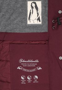 Bordeaux waterdichte jas interieur met grijze stofvoering, printdetails en functionele banden. Inclusief merklogo en verzorgingsinformatie.