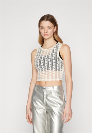Lace crop top featuring a patterned design in cream and black, with a sheer texture. Paired with metallic silver pants, reflecting light.