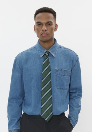 Jeanshemd mit Button-Down-Kragen, Brusttasche und blauer Farbe, kombiniert mit einer grün gestreiften Krawatte in verschiedenen Grüntönen und Grau.