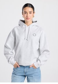 Sudadera gris con capucha, bolsillo frontal, cordón en la capucha y texto gráfico circular en el pecho. Tejido suave y diseño holgado.