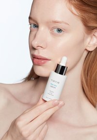 TIRTIR PHA 15% serum in een matte witte glazen fles met een pipet, zilveren dop en blauwe tekst, vastgehouden door een persoon met een heldere huid.