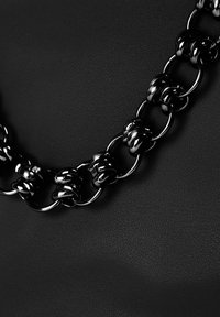 Cadena de metal negro con eslabones entrelazados y un acabado brillante, contra un fondo negro texturizado.