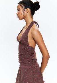 Haut halter marron avec des pois rouges, au design ajusté, ruché sur les côtés et avec un lien à l'arrière. Tissu lisse avec une texture légère.