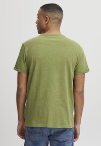 Grøn kortærmet t-shirt lavet af tekstureret stof. Har en afslappet pasform og optrækkede ærmer. Båret med blå jeans.