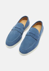 Plave mokasine od nubuka s tankim dizajnom, bijelim gumiranim potplatima i šavovima. Imaju bočni remen i glatku unutrašnjost.